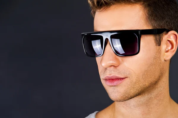 Hombre guapo en camiseta gris con sonrisa y gafas de sol —  Fotos de Stock