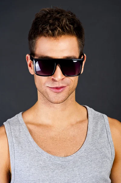 Hombre guapo en camiseta gris con sonrisa y gafas de sol — Foto de Stock