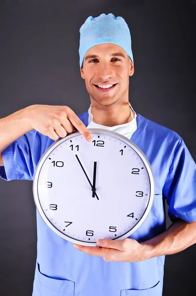 Chirurg mit Wanduhr vor dunklem Hintergrund — Stockfoto