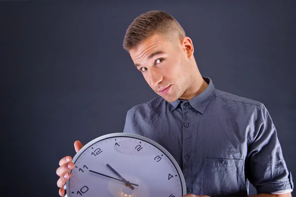 Mann hält Wanduhr vor dunklem Hintergrund — Stockfoto