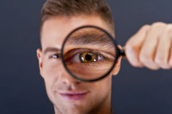 Uomo con lente di ingrandimento su sfondo scuro — Foto Stock