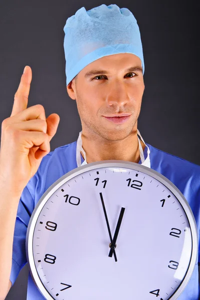 Surgeon with wall clock over dark background — Stock Photo, Image