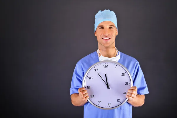 Surgeon with wall clock over dark background — Stock Photo, Image