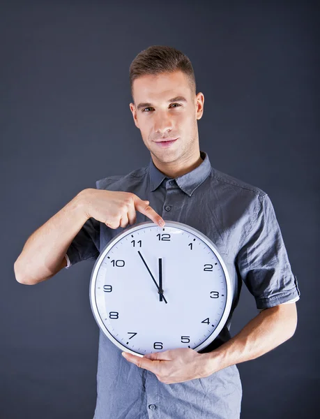 Uomo tenendo orologio da parete su sfondo scuro — Foto Stock