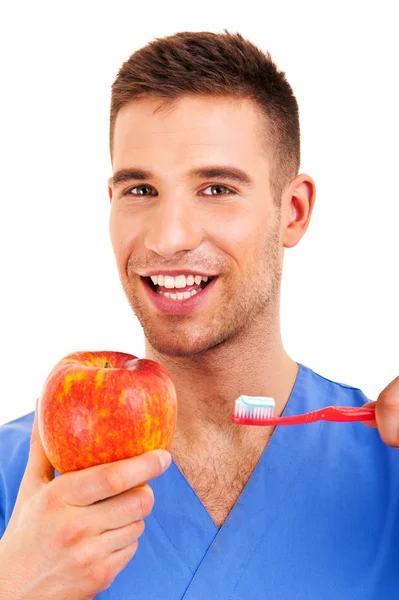 Ein junger Mann, der sich die Zähne putzt und den Apfel isoliert auf dem Rücken hält — Stockfoto