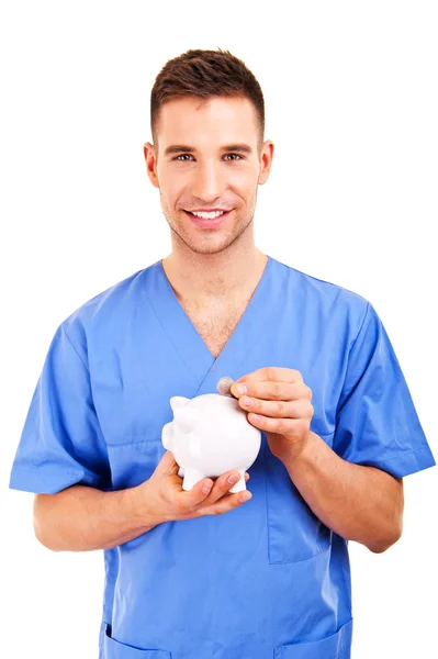 Médico masculino colocando moedas em um banco porquinho — Fotografia de Stock