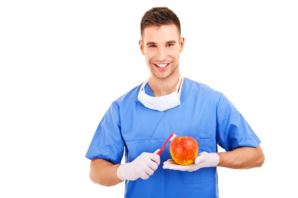 Handsome dentist brushing apple with toothbrush, isolated on — Stock Photo, Image