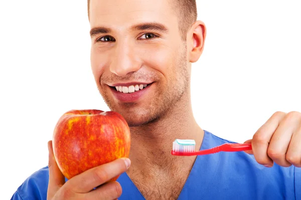 Un hombre joven cepillándose los dientes y sosteniendo manzana aislada en whi —  Fotos de Stock