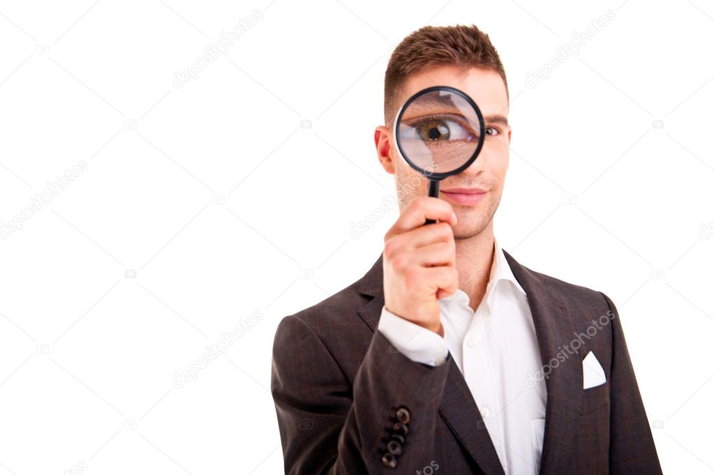 Young business man in suit looking to magnifying glass