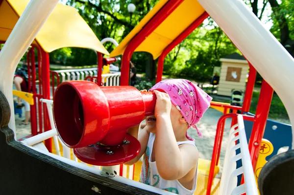 Kleines Mädchen blickt durch Teleskop auf Spielplatz — Stockfoto