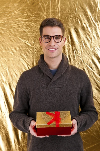Счастливый молодой человек несет подарок на золотом фоне — стоковое фото