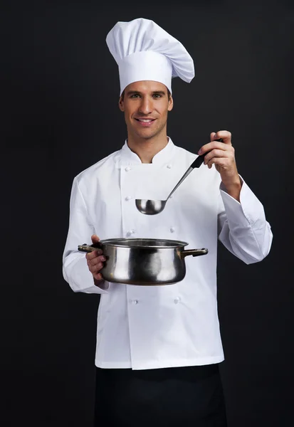 Cook against dark background holding pot and spoon — Stock Photo, Image