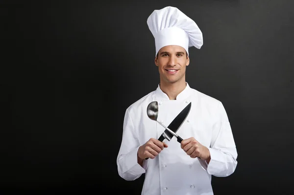 Chef-kok koken tegen donkere achtergrond lachend met hoed holdinf lepel — Stockfoto