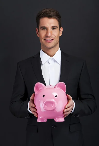 Empresário segurando porquinho banco contra fundo escuro — Fotografia de Stock