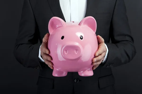 Businessman holding piggy bank against dark background — Stock Photo, Image