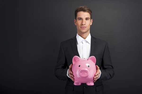 Biznesmen posiadania piggy bank ciemnym tle — Zdjęcie stockowe