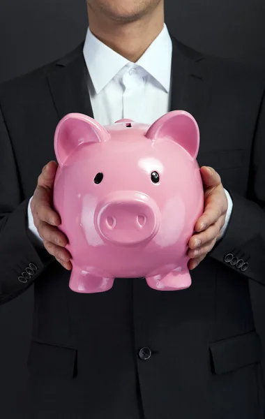 Empresário segurando porquinho banco contra fundo escuro — Fotografia de Stock