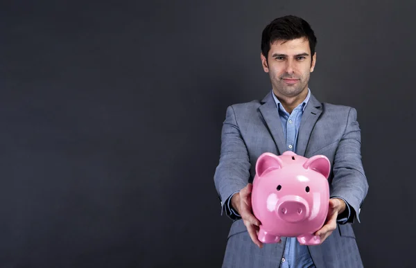 Geschäftsmann mit Sparschwein vor dunklem Hintergrund — Stockfoto