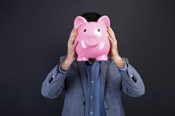 Portrait of young man holding a piggy bank against a grunge back — Stock Photo, Image