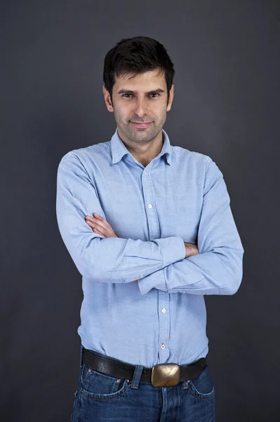 Joven hombre guapo sonriendo sobre fondo gris con los brazos cruzados — Foto de Stock