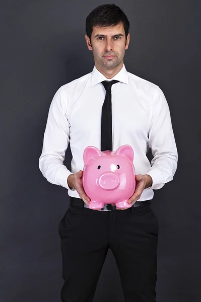 Young man with piggy bank (money box), on dark background — Stock Photo, Image