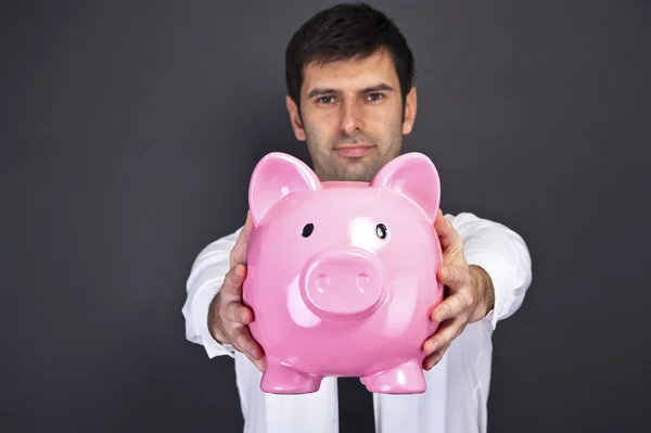 Portrait of young man holding a piggy bank against a grunge back — Stock Photo, Image