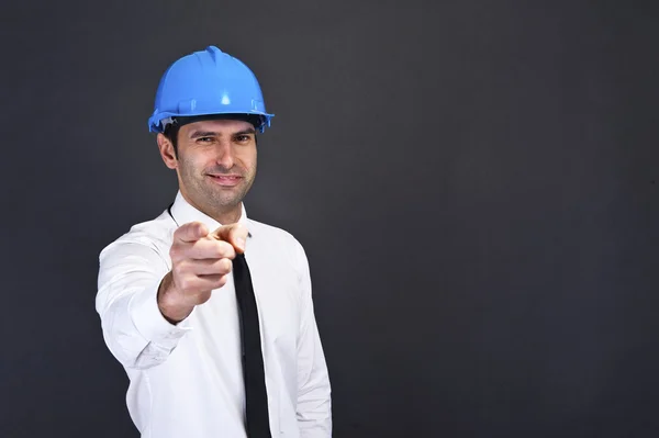 Young construction worker in hard hat on gray background pointin — Stock Photo, Image