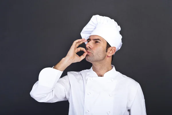 Männerkoch küsst Finger vor grauem Hintergrund — Stockfoto