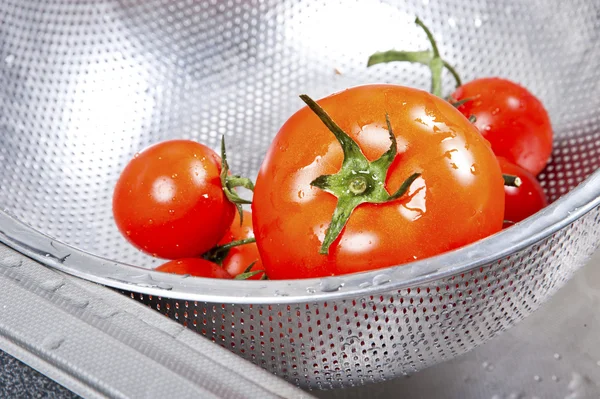 Fresh tomatoes in colander splashing in water — Stock Photo, Image