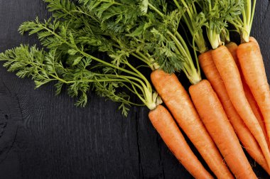 Bunch of fresh carrots with green leaves over wooden background. clipart