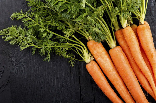 Bunch of fresh carrots with green leaves over wooden background.