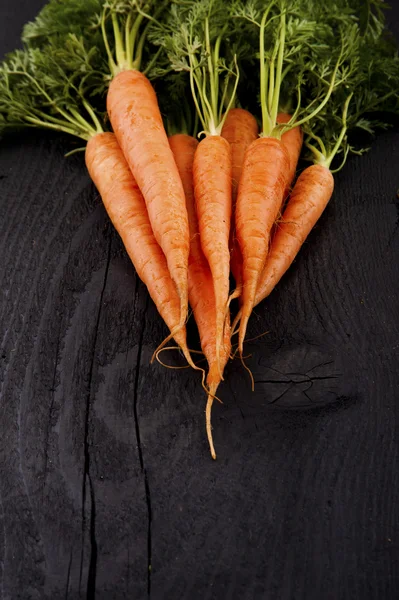 Куча свежей моркови с зелеными листьями на деревянном фоне . — стоковое фото