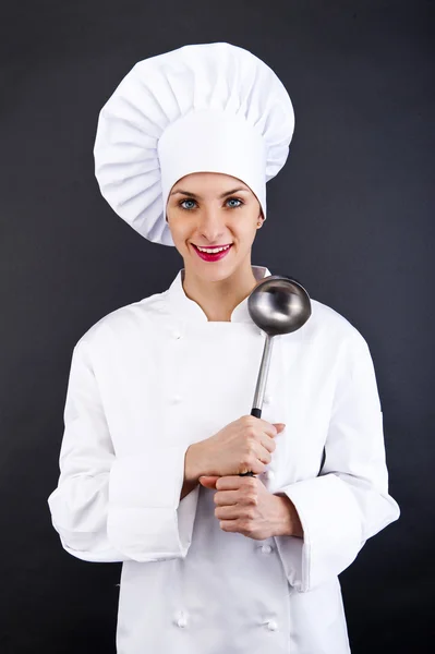 Porträtt av ung kvinna kock med sked på mörk bakgrund — Stockfoto