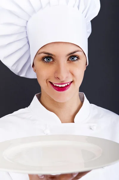 Woman cook or chef serving empty plate and smiling happy — Stock Photo, Image