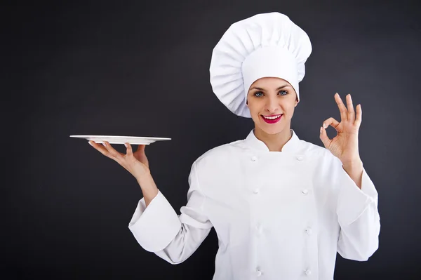 Woman cook or chef serving empty plate and smiling happy — Stock Photo, Image