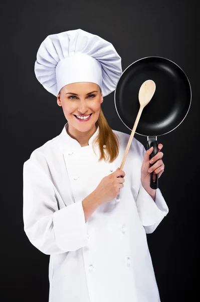 Beautiful blonde woman chef holding pan on white dark background — Stock Photo, Image