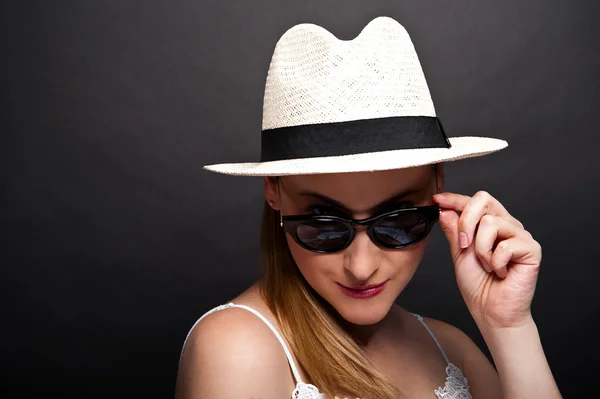 Frau mit Hut und Sonnenbrille vor dunklem Hintergrund Stockbild