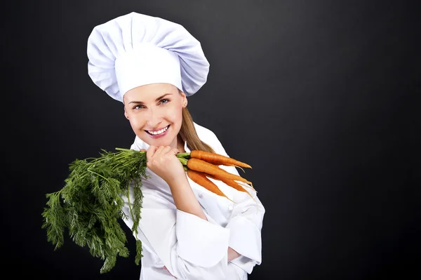 Female cook in white uniform with bunch of carrots — Stock Photo, Image