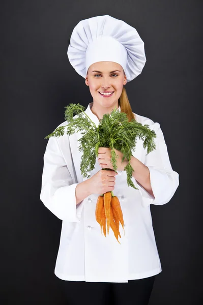 Женщина повар в белой форме с кучей моркови — стоковое фото