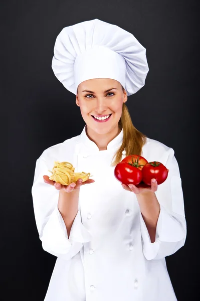 Kvinna kocken över mörk bakgrund med tomater och nudlar pasta — Stockfoto