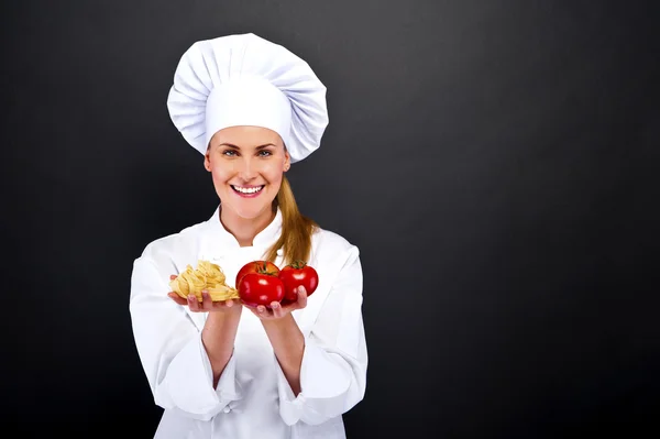 Kvinna kocken över mörk bakgrund med tomater och nudlar pasta — Stockfoto