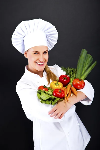 Woman chef make hand heart sign with tomato over dark background — Stock Photo, Image