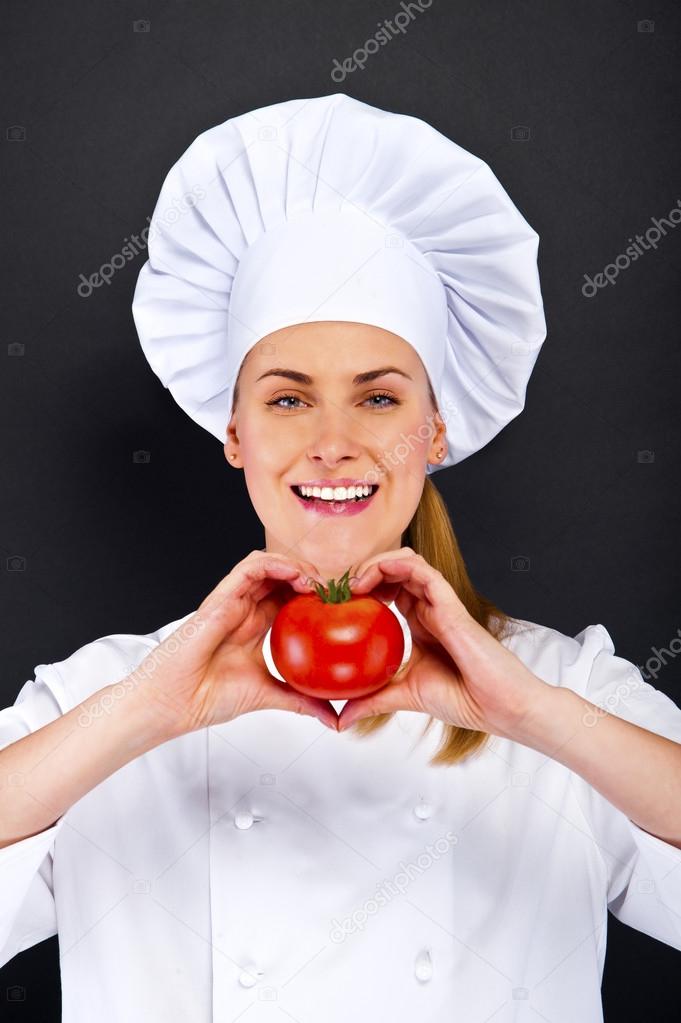 woman chef make hand heart sign with tomato over dark background