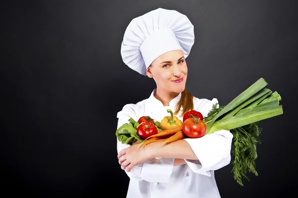 Woman chef make hand heart sign with tomato over dark background — Stock Photo, Image