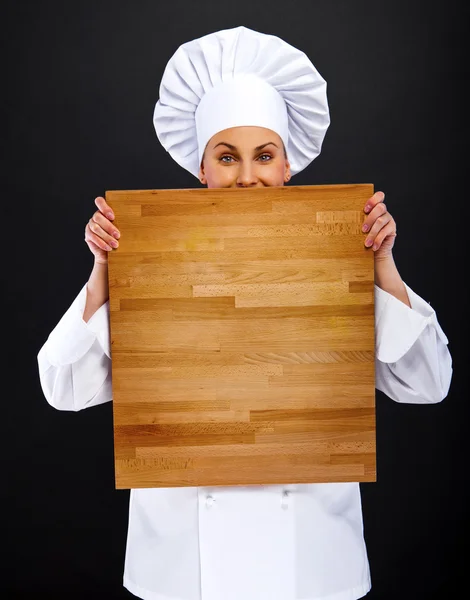 Woman chef holding wooden board pionting with smile — Stock Photo, Image