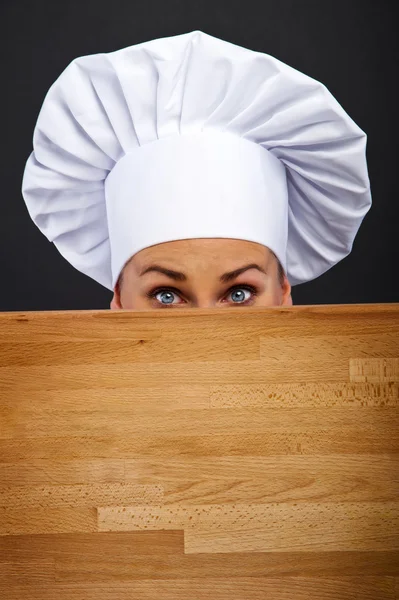 Chef donna su sfondo scuro in shock dietro bordo di legno — Foto Stock
