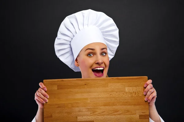 Chef mujer sobre fondo oscuro en shock detrás de tablero de madera — Foto de Stock