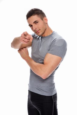 Muscle young guy smiling and pointing at you against white backg