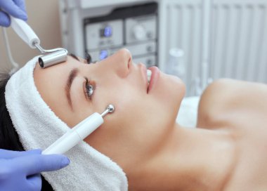 Kozmetik uzmanı bu aleti güzellik salonundaki genç ve güzel bir kadının mikro-akım terapisi için bir prosedür haline getiriyor. Kozmetoloji ve profesyonel cilt bakımı.