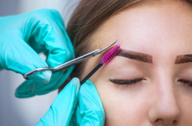 Master makeup corrects, gives shape to and cut with scissors previously painted with henna eyebrows in a beauty salon. Professional care for face.